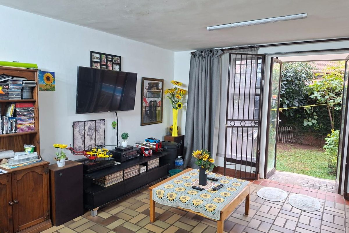A living room featuring tiled flooring and direct access to the rear garden through double glass doors with an integrated security gate.