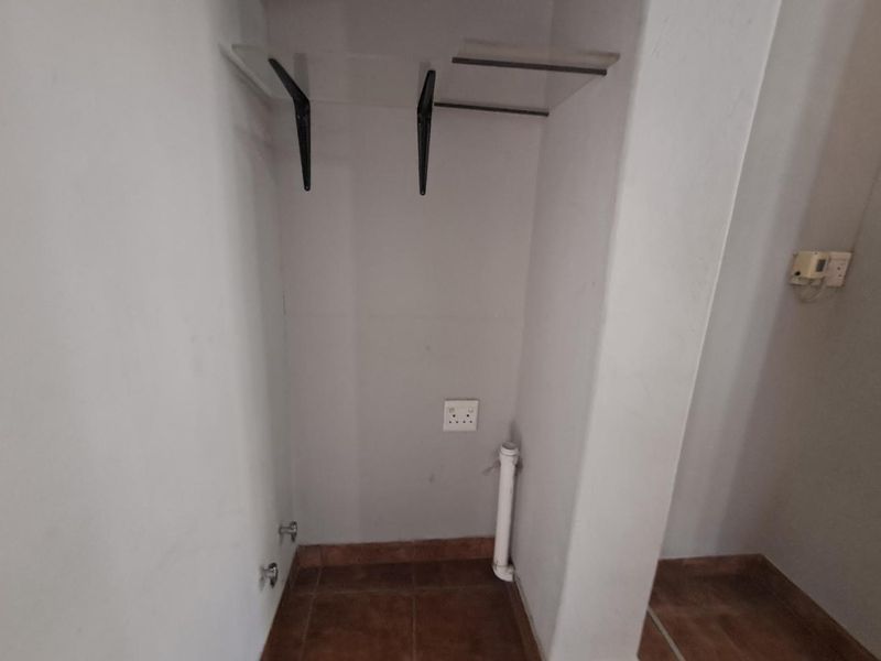 A functional laundry alcove featuring tiled flooring, dedicated plumbing connections, and an electrical outlet, ready for appliance installation.