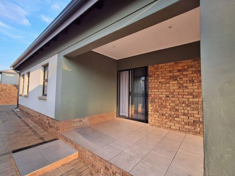 A well-maintained covered patio featuring tiled flooring, exposed brick accents, and a sliding glass door entrance.