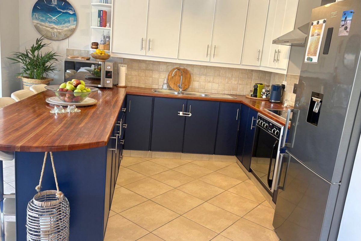 A well-maintained kitchen featuring contrasting navy and white cabinetry, warm wooden countertops, tiled backsplash, and integrated appliances with tiled flooring.