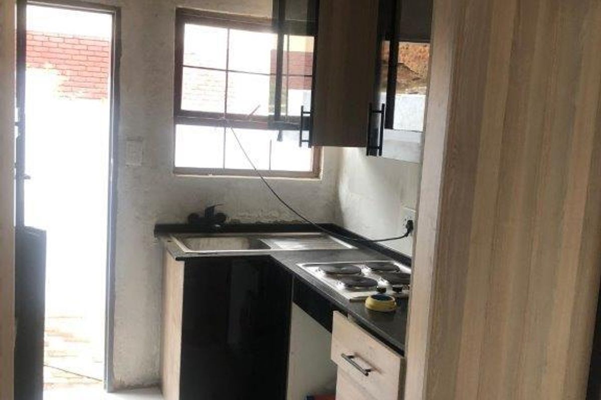 Compact kitchen area featuring modern cabinetry, a built-in hob, and sink, currently undergoing renovation with unfinished walls and ceiling.