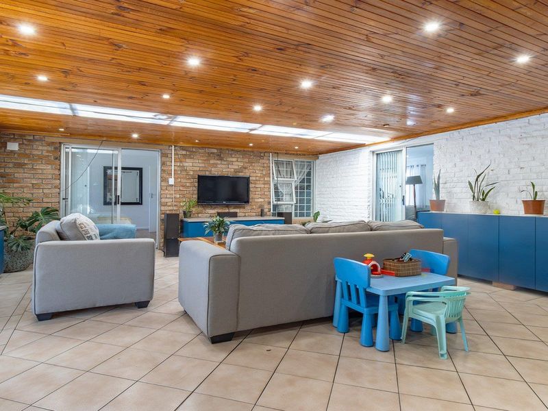Spacious living room featuring a timber-clad ceiling with recessed lighting, a skylight, exposed brick walls, and tiled flooring with integrated cabinetry.