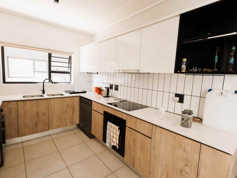 Modern kitchen featuring wood-grain cabinetry, white stone countertops, a double basin sink, and integrated appliances with a clean tiled backsplash.