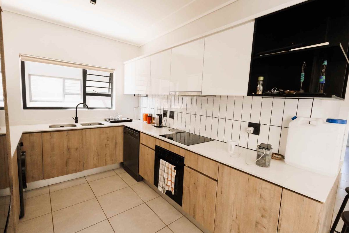 Modern kitchen featuring wood-grain cabinetry, white stone countertops, a double basin sink, and integrated appliances with a clean tiled backsplash.