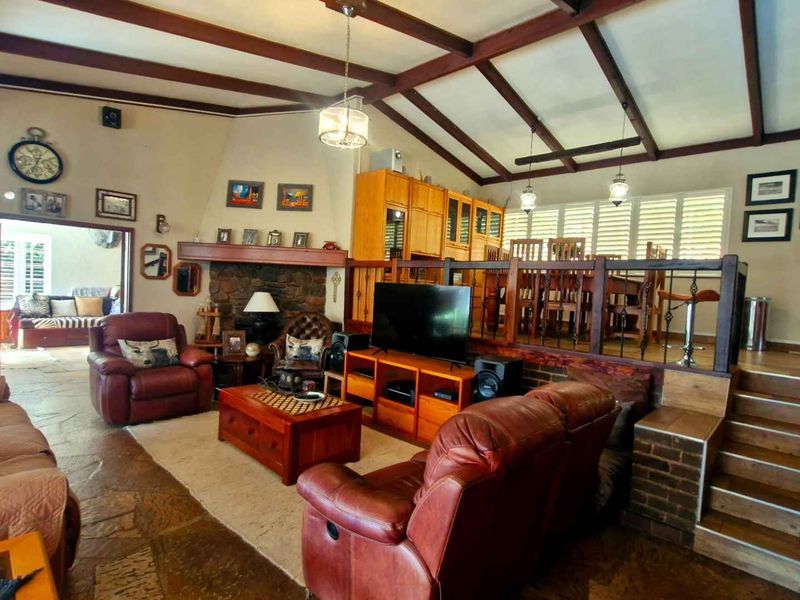 Spacious open-plan living and dining area featuring exposed timber ceiling beams, a stone fireplace, and split-level flooring with a timber staircase.