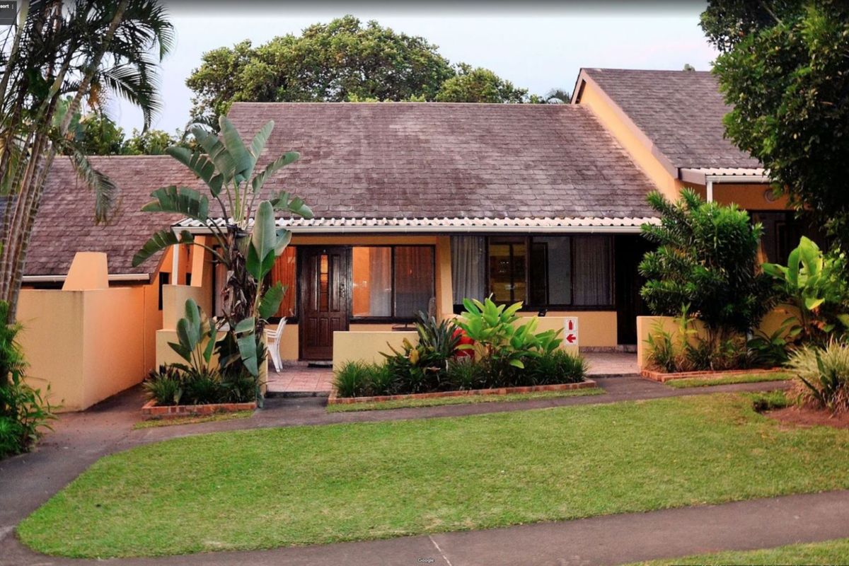 Exterior view of a single-story apartment unit featuring a tiled roof, paved patio area, and established garden surroundings.