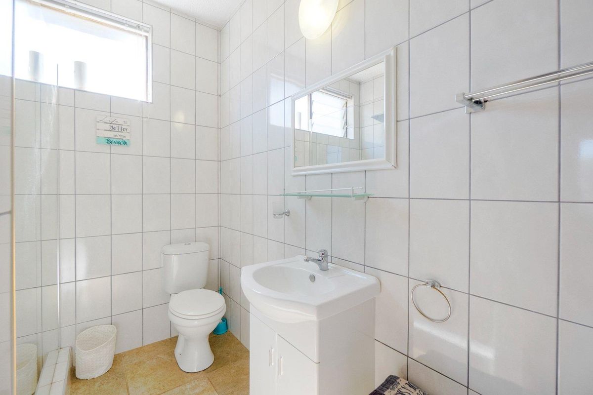 A functional bathroom featuring white wall tiles, a pedestal vanity with integrated basin, a toilet, and a wall-mounted mirror.