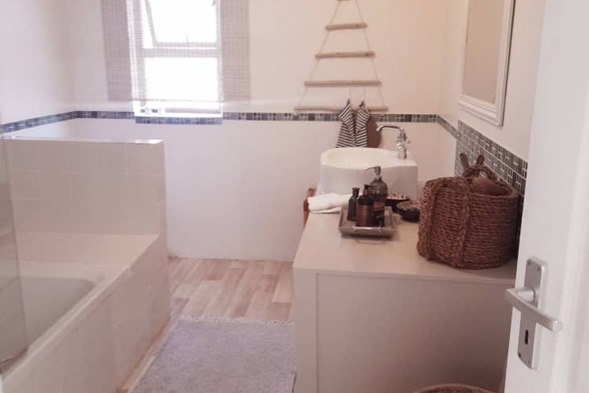 A functional bathroom featuring a built-in bathtub, a vanity unit with a basin, and tiled splashback detailing.