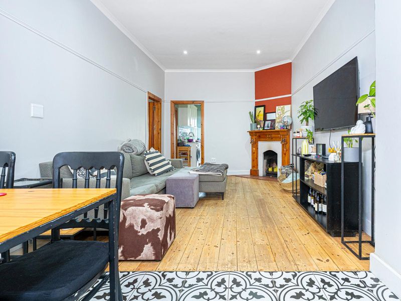 Open plan living area featuring original wooden flooring, a decorative fireplace mantel, and a transition to patterned tiled flooring near the dining space.