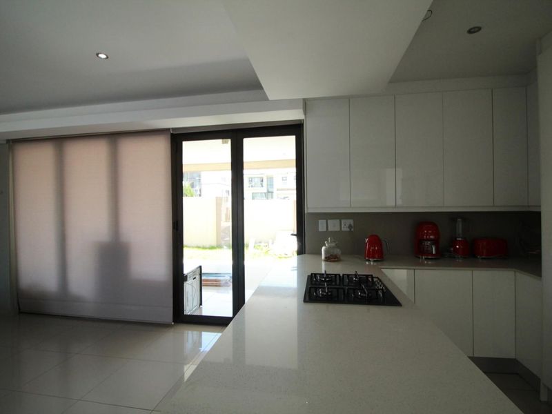 Modern kitchen featuring sleek white cabinetry, stone countertops, a built-in gas hob, and direct access to the outdoor area through sliding glass doors.