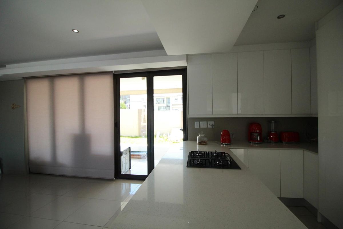 Modern kitchen featuring sleek white cabinetry, stone countertops, a built-in gas hob, and direct access to the outdoor area through sliding glass doors.
