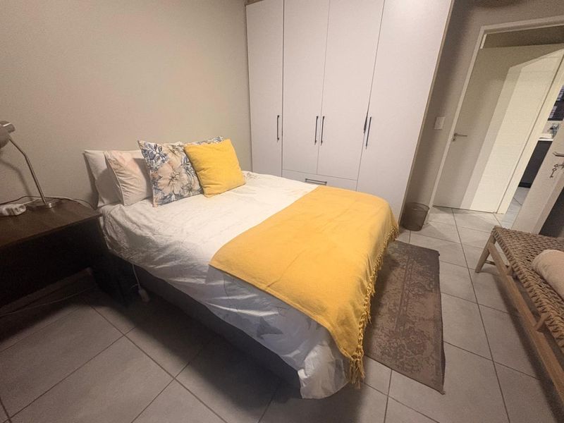 A well-maintained bedroom featuring neutral tiled flooring and a spacious built-in wardrobe with clean white cabinetry.