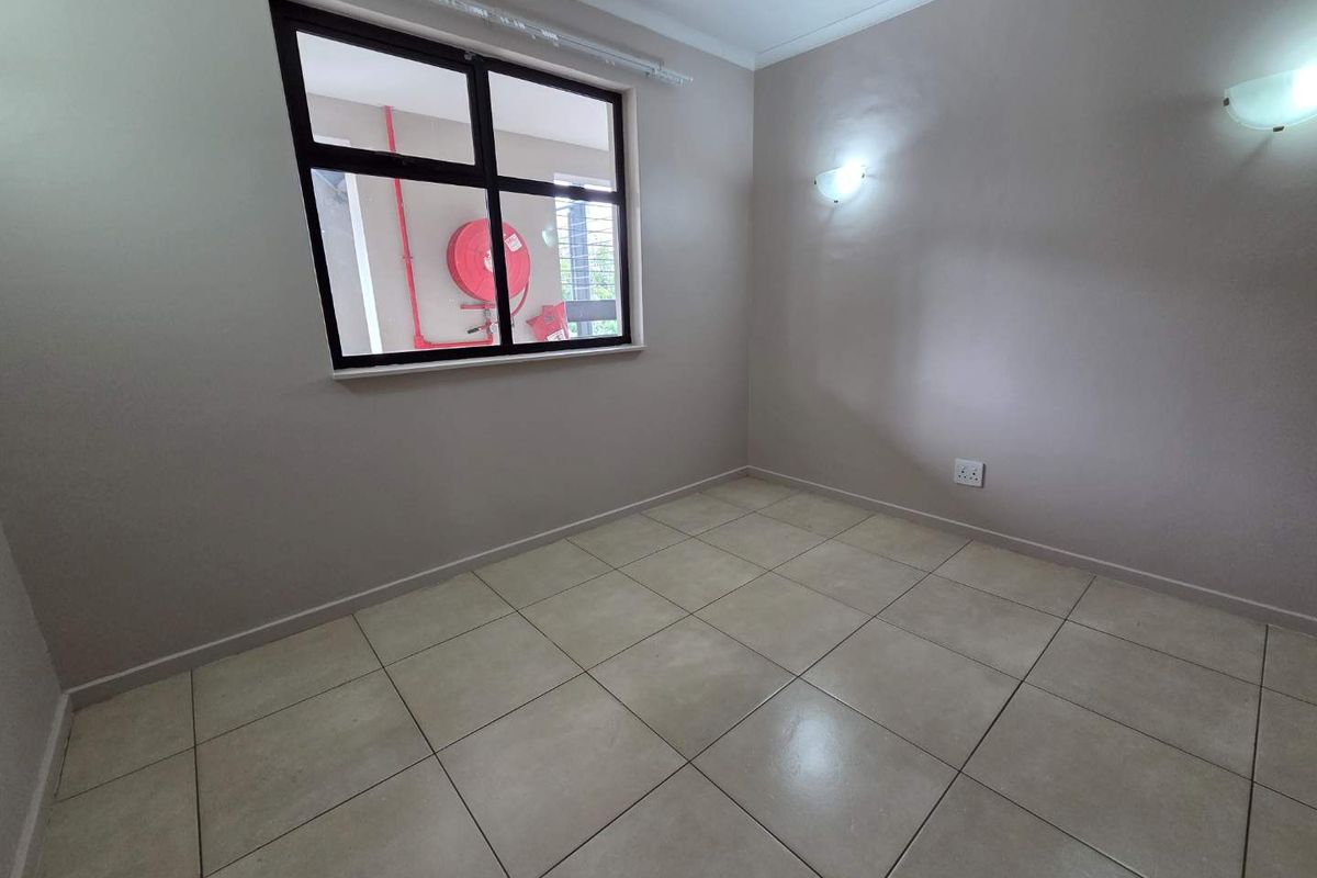 A clean, empty bedroom featuring neutral tiled flooring, painted walls, and wall-mounted light fixtures.