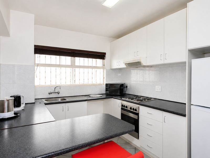 A functional kitchen featuring white cabinetry, dark laminate countertops, built-in oven with gas hob, and a tiled backsplash with security bars on the window.