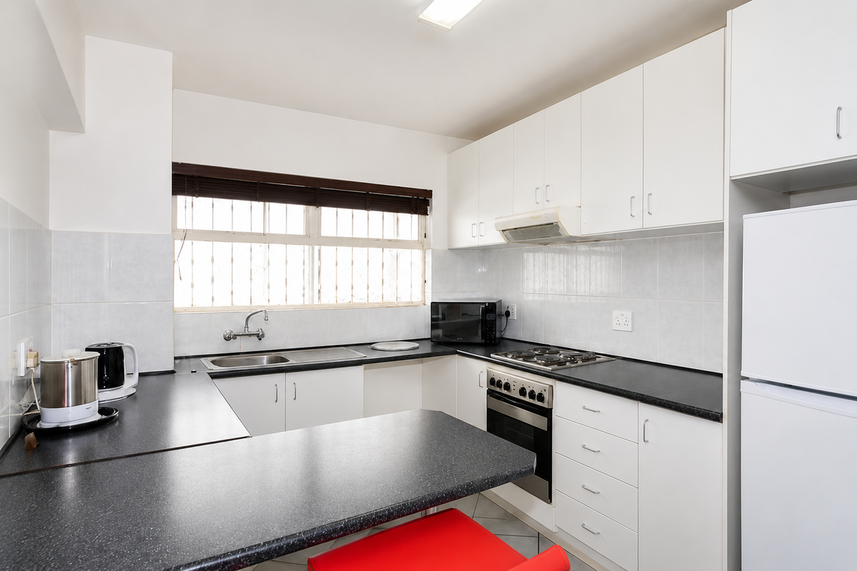 A functional kitchen featuring white cabinetry, dark laminate countertops, built-in oven with gas hob, and a tiled backsplash with security bars on the window.