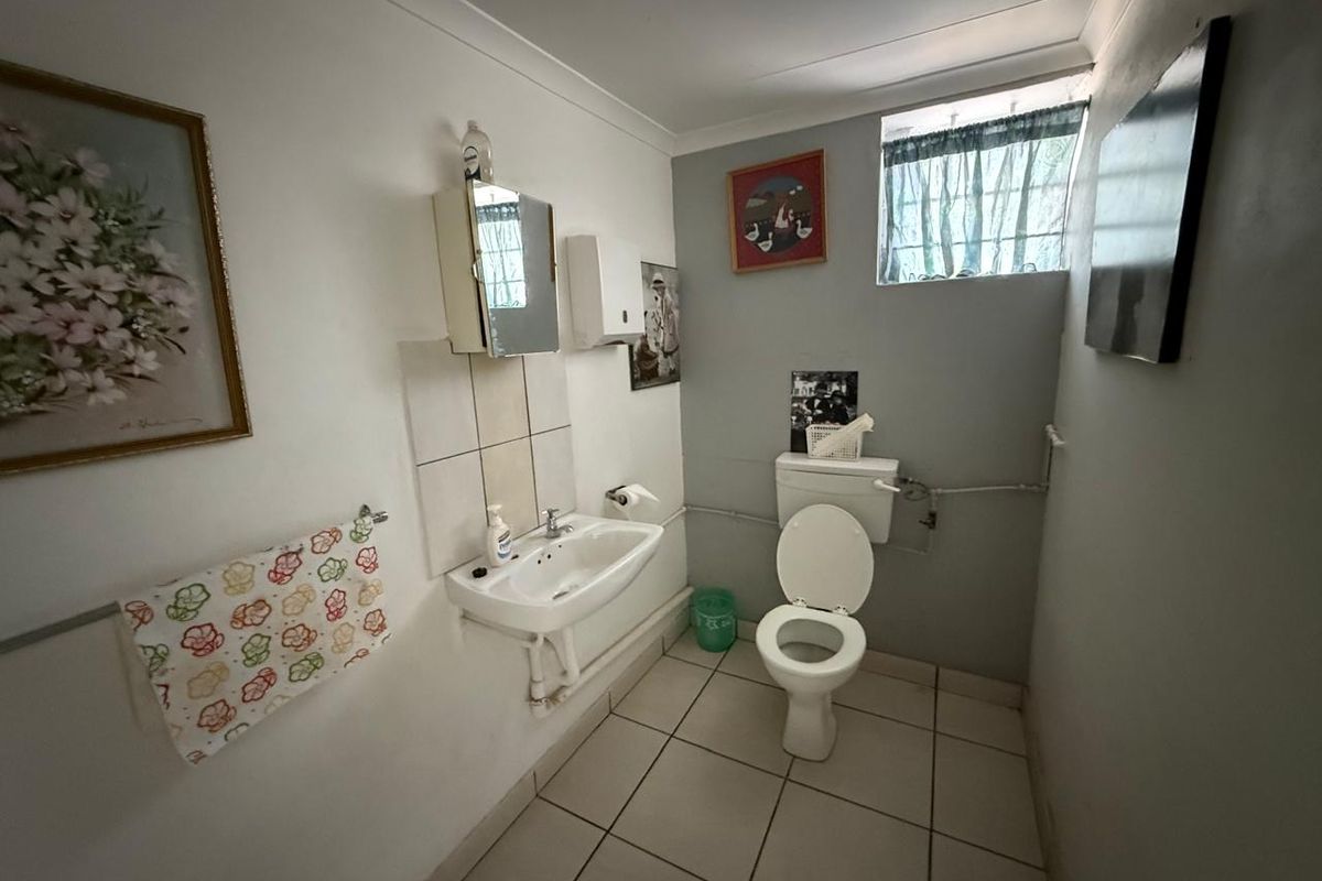 A functional bathroom featuring a wall-mounted basin, toilet, tiled flooring, and a small window for natural light.