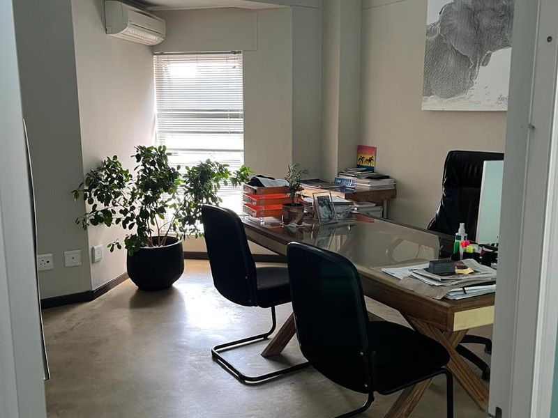 A bright, modern office space featuring polished concrete floors, a high transom window for natural light, and a wall-mounted air conditioning unit.