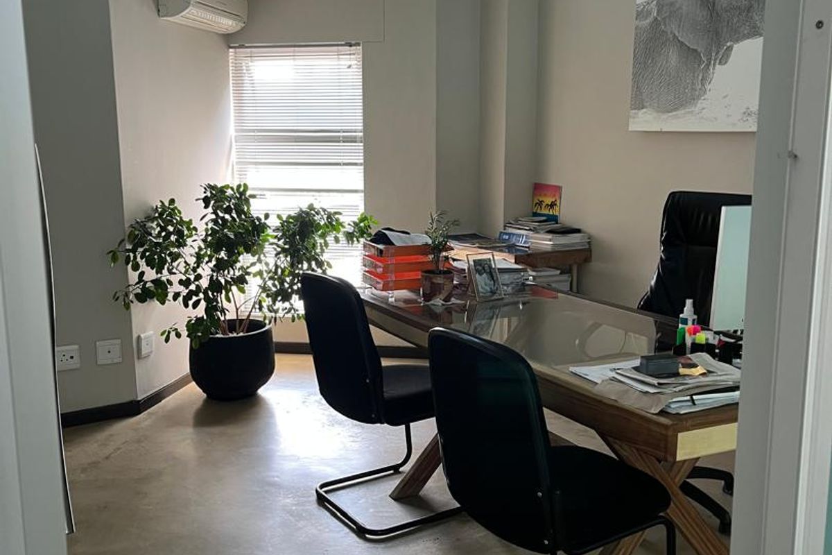 A bright, modern office space featuring polished concrete floors, a high transom window for natural light, and a wall-mounted air conditioning unit.