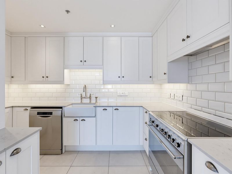Modern kitchen featuring white shaker-style cabinetry, subway tile backsplash, stone countertops, an apron-front sink, and high-quality stainless steel appliances.
