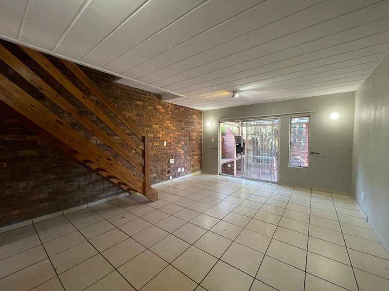 Spacious living area featuring an exposed brick feature wall, wooden staircase, tiled flooring, and direct access to the outdoor patio through sliding glass doors.