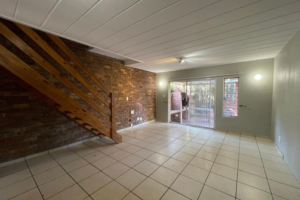 Spacious living area featuring an exposed brick feature wall, wooden staircase, tiled flooring, and direct access to the outdoor patio through sliding glass doors.