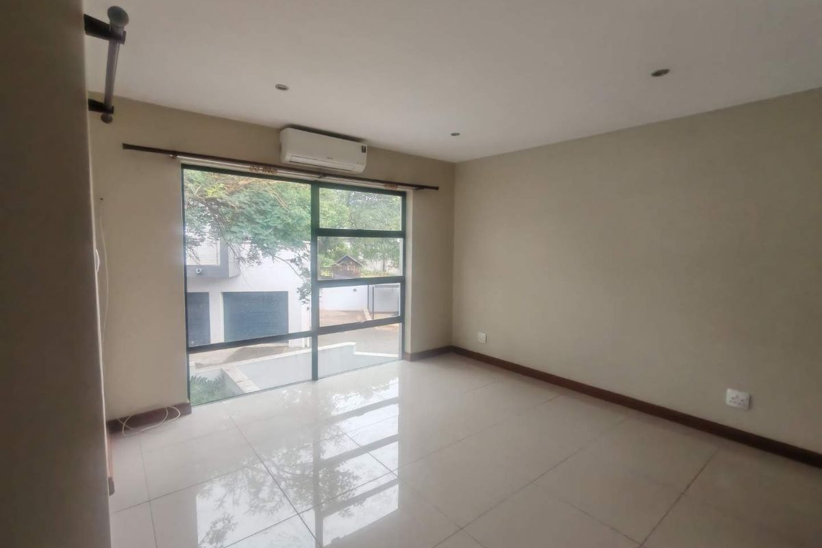 A bright, empty bedroom featuring large windows, tiled flooring, and a wall-mounted air conditioning unit.