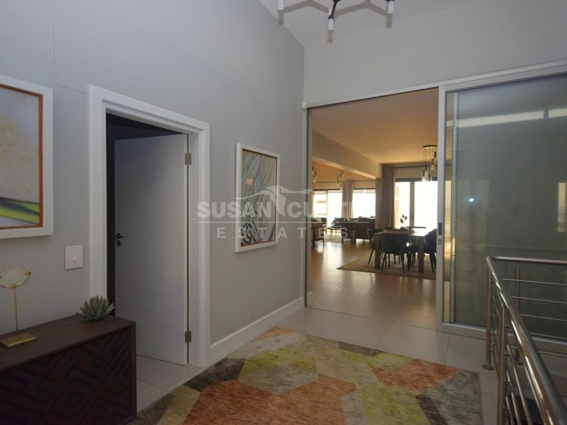 A bright, modern hallway featuring tiled flooring, a stainless steel balustrade, and a large sliding glass door leading into the main living area.