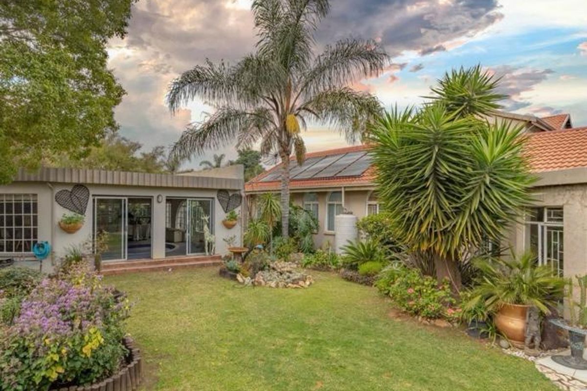 A well-maintained rear garden featuring a lawn, mature landscaping, solar panels on the roof, and a patio area with sliding glass doors.