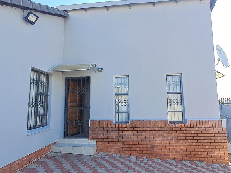Front exterior view of the house featuring a paved driveway, brick facade detailing, and security gates on the entrance and windows.
