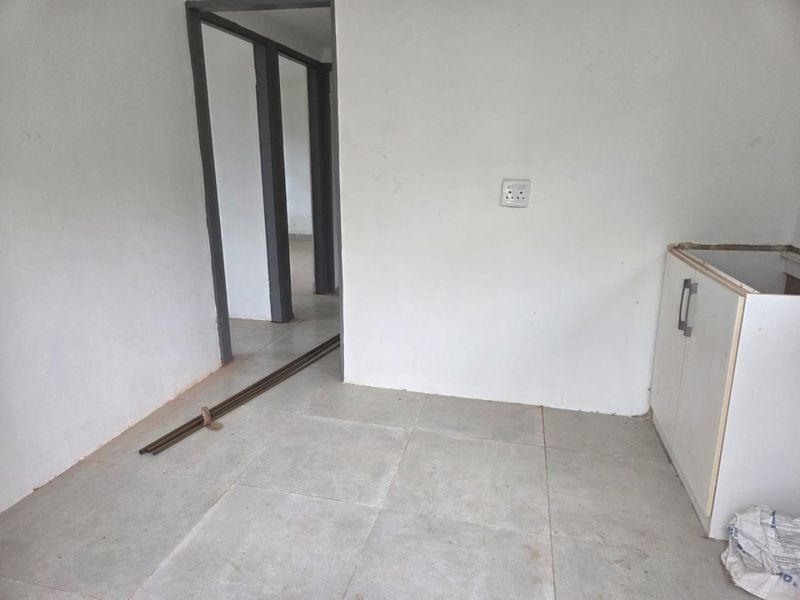 An unfinished kitchen area featuring tiled flooring and base cabinetry, currently awaiting countertop installation and final finishes.