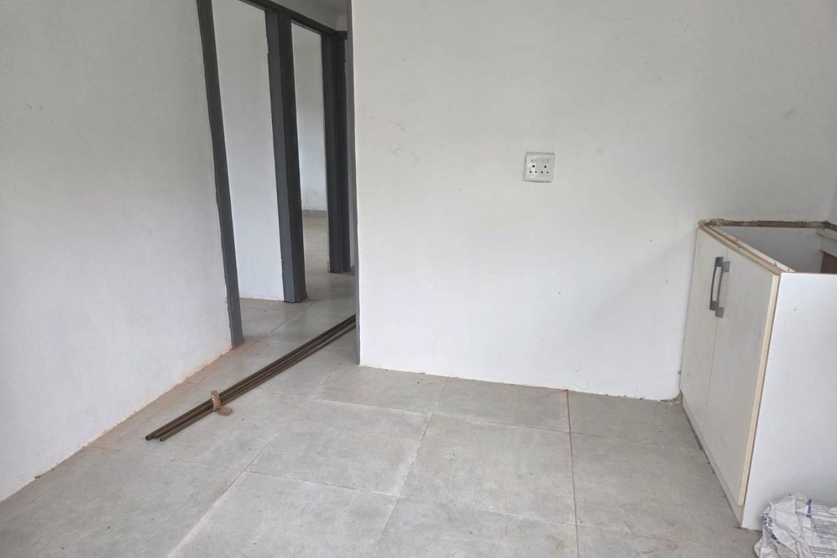 An unfinished kitchen area featuring tiled flooring and base cabinetry, currently awaiting countertop installation and final finishes.