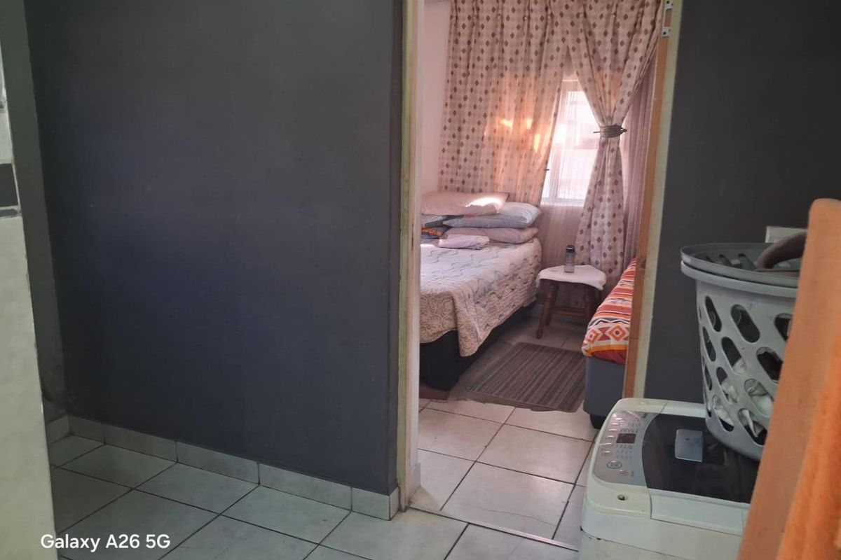 A view from a tiled hallway into a bedroom featuring dark painted walls and tiled flooring with visible wear.