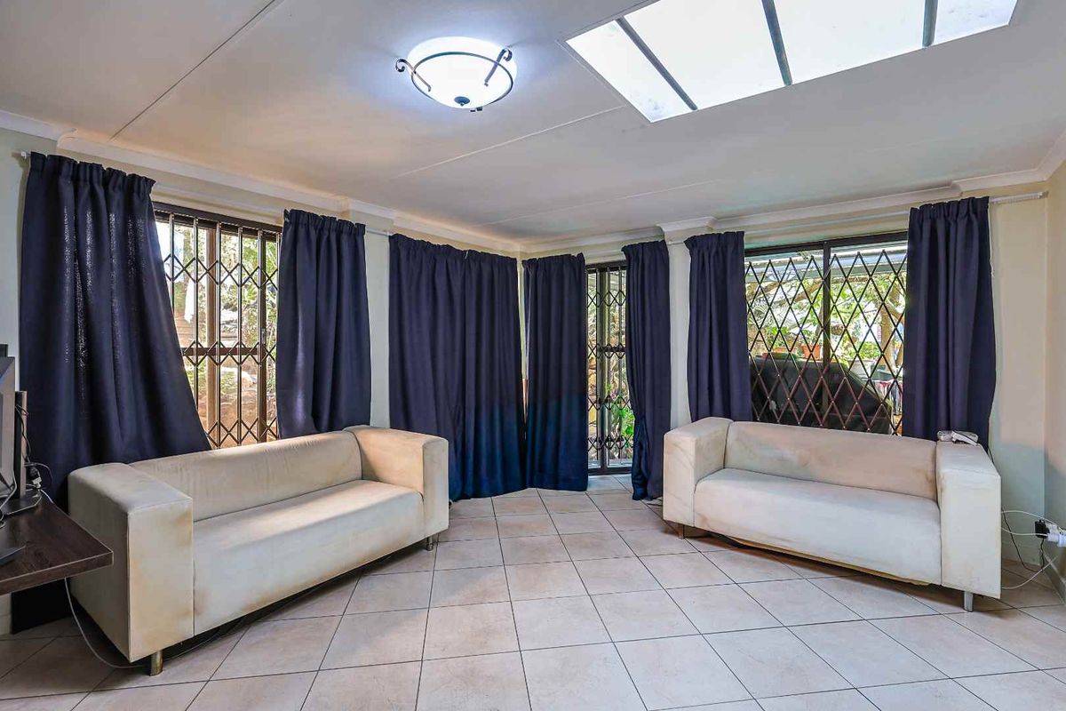 A bright living room featuring large windows with security gates, tiled flooring, and a skylight, providing ample natural light.