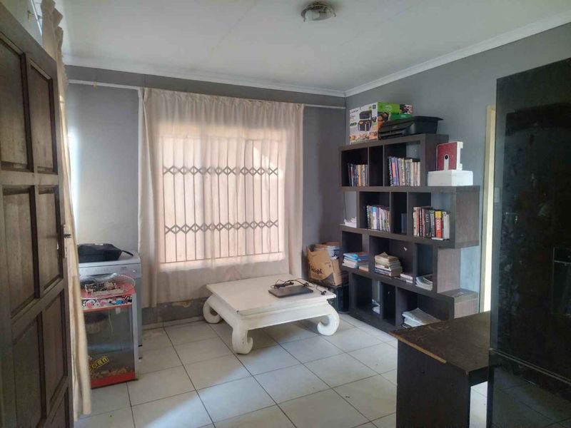 A living area featuring tiled flooring and a security gate on the window, currently showing signs of wear and needing cosmetic updates.