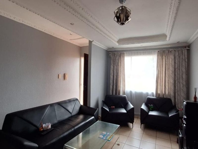 A living room featuring tiled flooring, coved ceiling details, and recessed lighting, providing a functional space for relaxation.