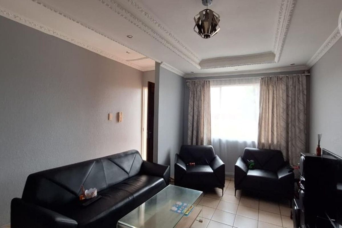A living room featuring tiled flooring, coved ceiling details, and recessed lighting, providing a functional space for relaxation.