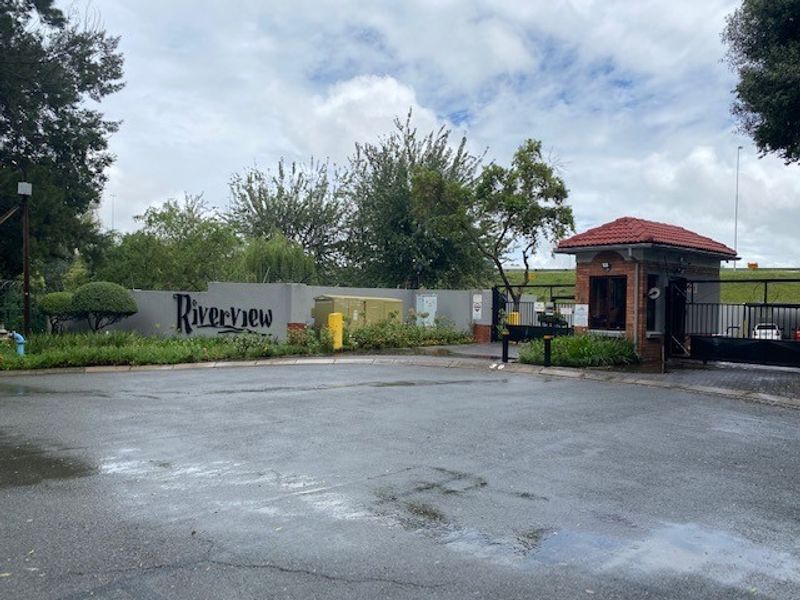 The entrance to Riverview complex featuring a secure gatehouse, perimeter wall, and paved driveway access.