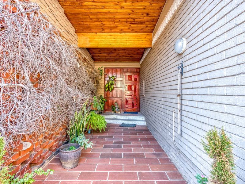 Covered entrance porch featuring a timber ceiling, brick walls, and tiled flooring leading to a solid timber front door.