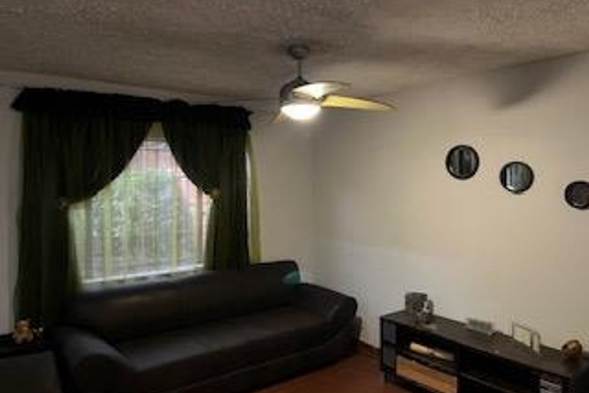 A living room featuring a ceiling fan, wood-style flooring, and a window with curtains.