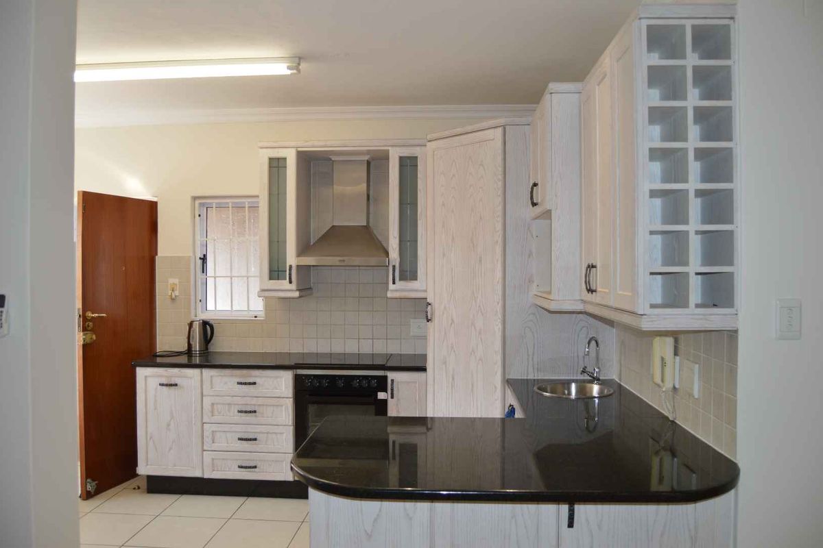 A functional kitchen featuring light wood-grain cabinetry, dark granite countertops, integrated oven, extractor fan, and a convenient breakfast bar area.
