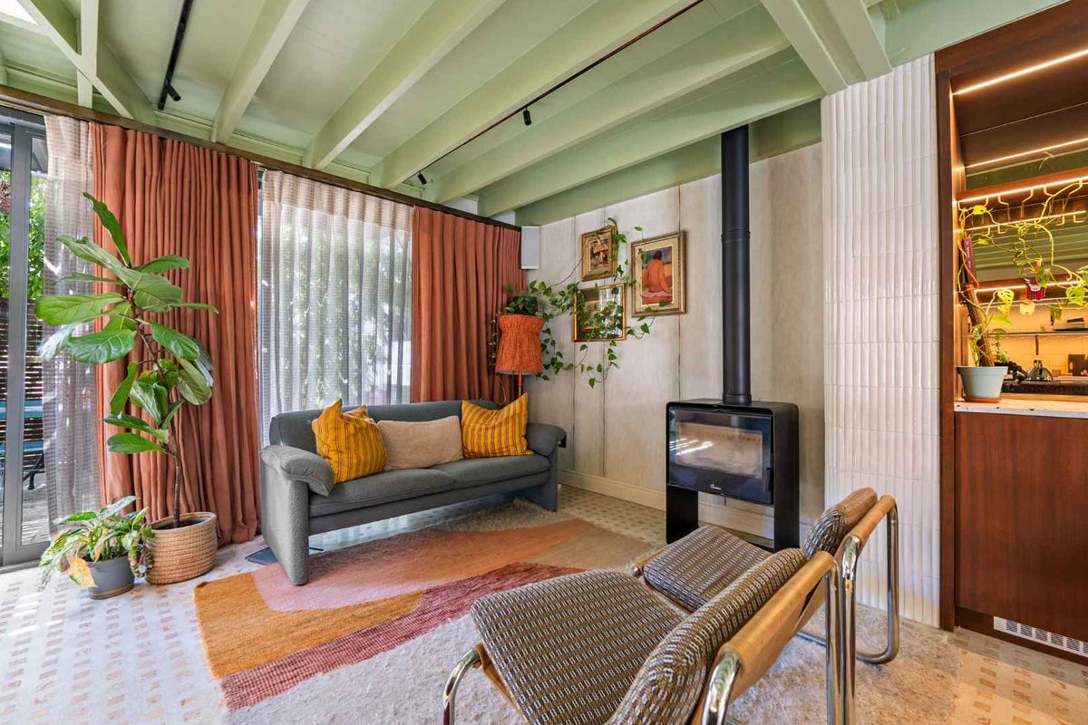 A stylish living room featuring an exposed beam ceiling, a modern freestanding wood-burning fireplace, and integrated cabinetry with elegant tiled wall accents.