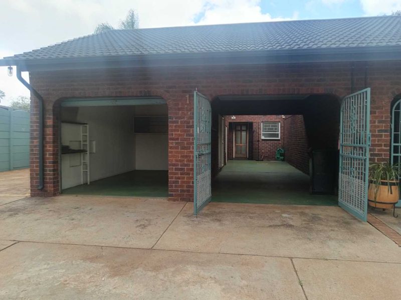 A double garage featuring brick construction, a tiled roof, and metal security gates, with a concrete driveway and built-in storage shelving.