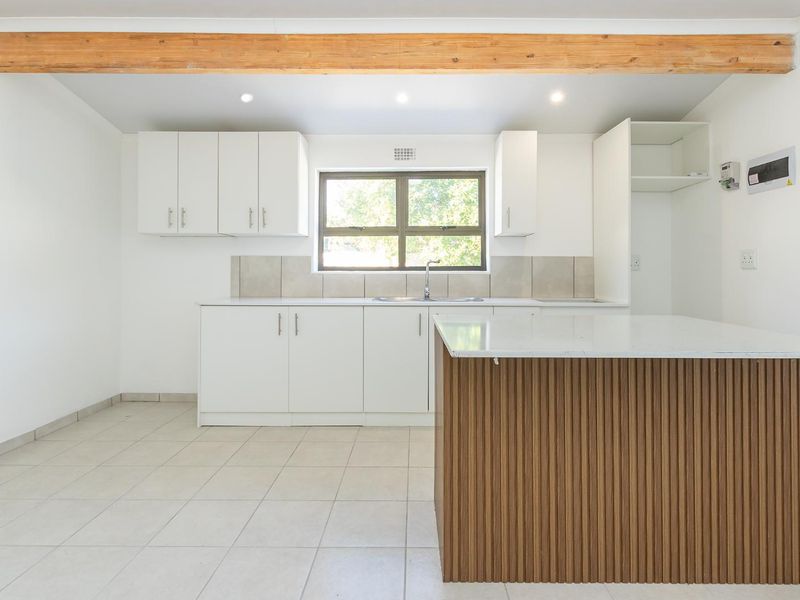 Modern kitchen featuring white cabinetry, a timber-accented island, stone countertops, tiled backsplash, and an exposed wooden ceiling beam in a bright, open space.