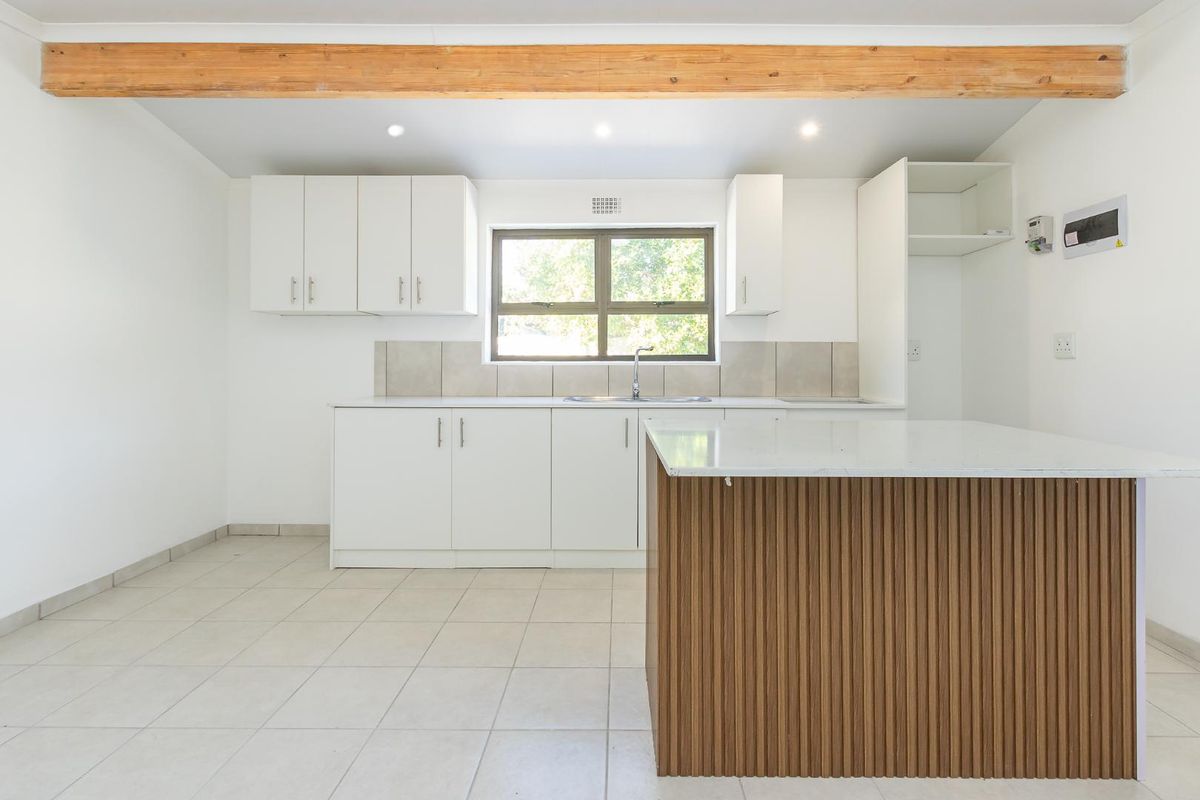 Modern kitchen featuring white cabinetry, a timber-accented island, stone countertops, tiled backsplash, and an exposed wooden ceiling beam in a bright, open space.