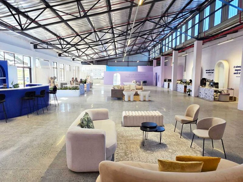 Spacious open-plan industrial warehouse conversion featuring polished concrete floors, exposed steel roof trusses, and a built-in bar area with modern architectural arches.