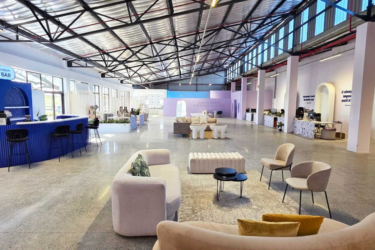Spacious open-plan industrial warehouse conversion featuring polished concrete floors, exposed steel roof trusses, and a built-in bar area with modern architectural arches.
