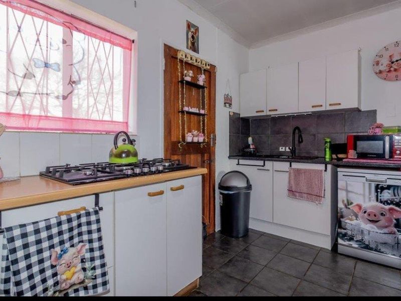 Compact kitchen featuring white cabinetry, dark tiled splashback, gas hob, and tiled flooring, offering a functional layout with potential for modern updates.