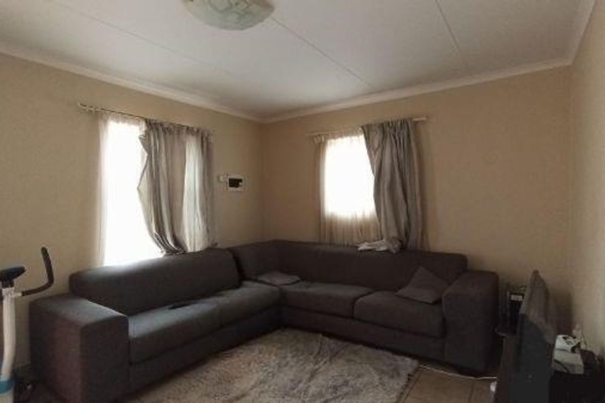 A functional living room featuring tiled flooring, neutral wall tones, and natural light through two windows with fitted curtain tracks.