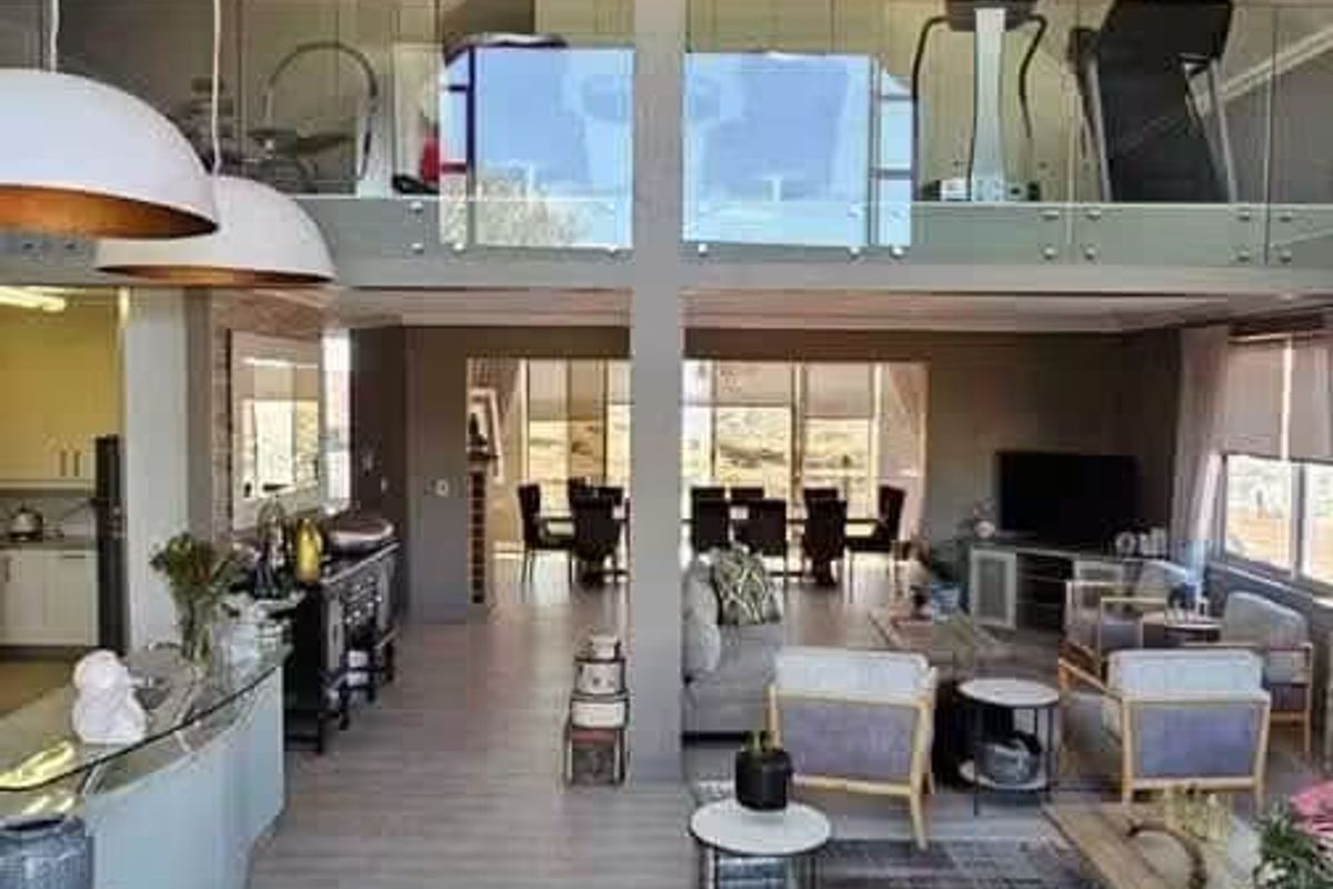 Spacious open-plan living area featuring a vaulted ceiling, mezzanine level with glass balustrade, and modern laminate flooring throughout.