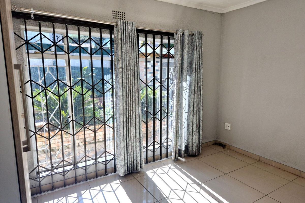 An empty living room featuring tiled flooring and sliding glass doors with integrated security gates, providing access to the exterior.